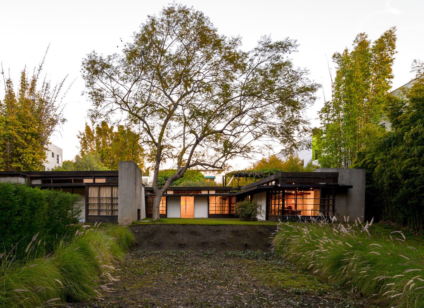 Modern house with large windows surrounded by trees and garden, featuring a central courtyard at dusk.