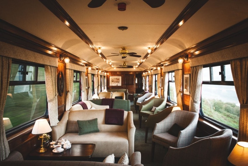 Luxurious train interior with elegant seating, warm lighting, and large windows offering scenic views.
