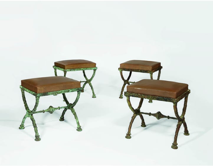 Four bronze patinated metal stools with brown leather seats on a white background.