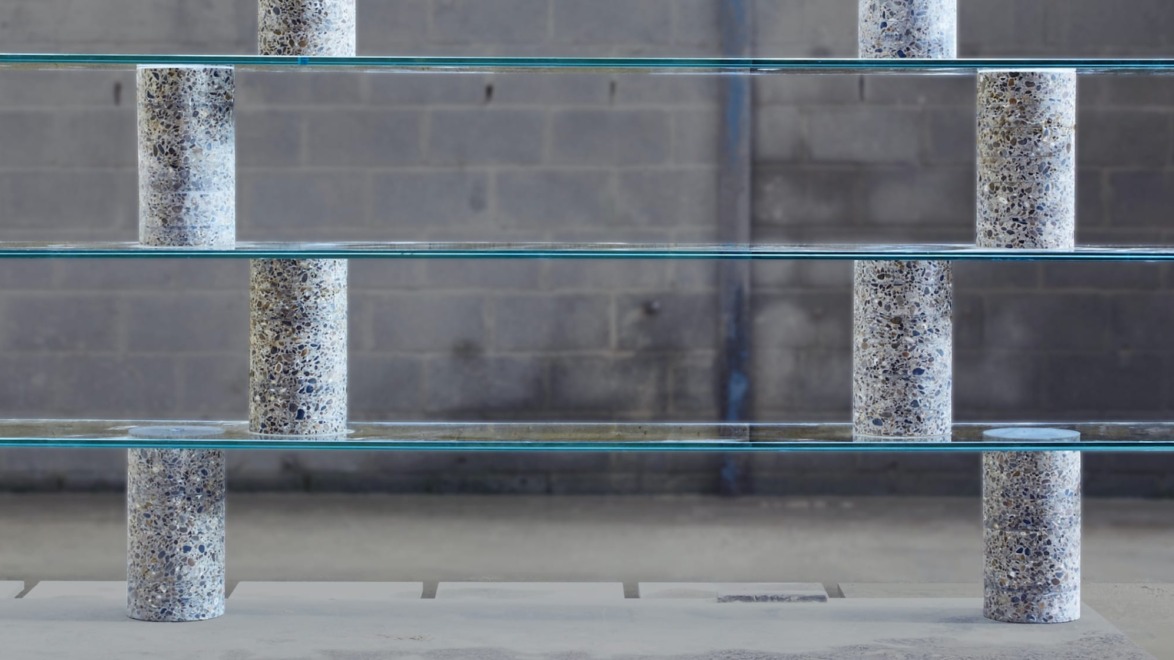Modern glass shelving unit with cylindrical concrete supports in an industrial setting.