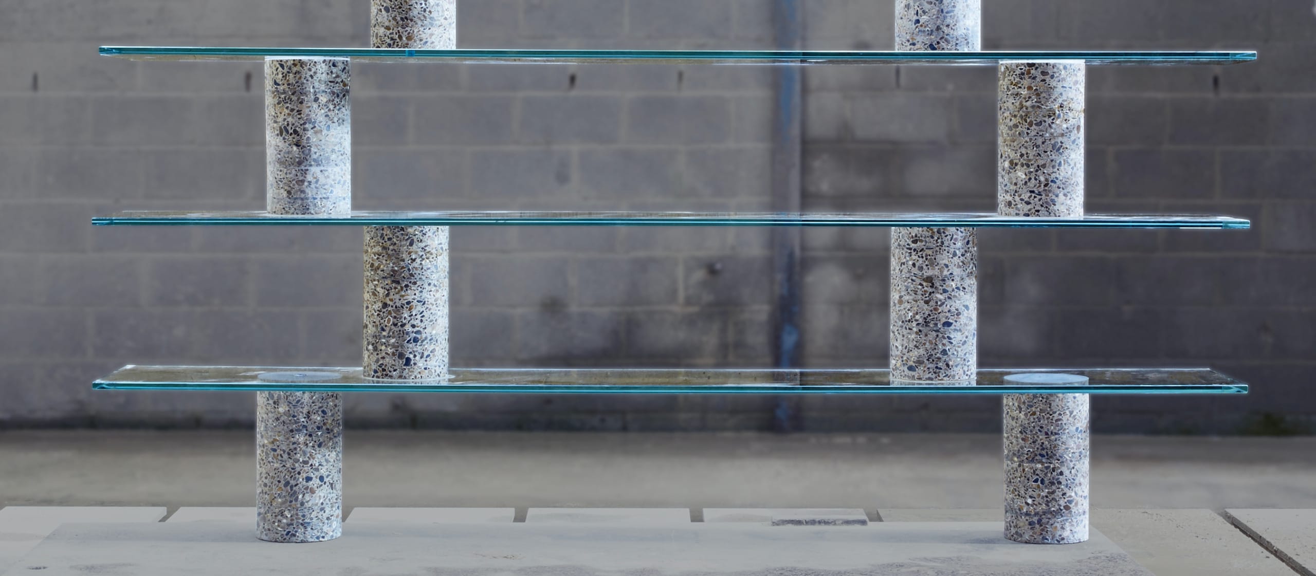 Modern glass shelving unit with cylindrical concrete supports in an industrial setting.