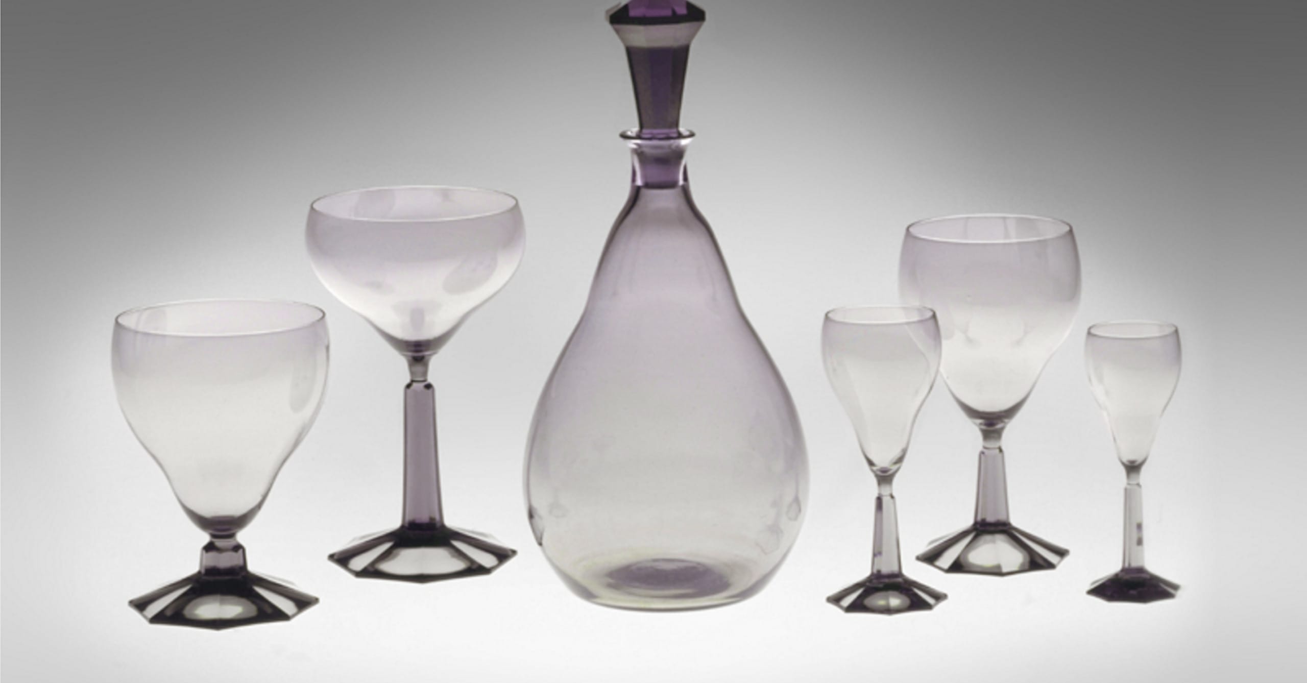Set of elegant glassware featuring a central decanter and five matching glasses on a neutral background.