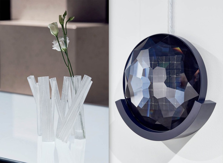 Modern art piece with geometric crystal structure on wall beside a vase of white flowers on a glossy surface.