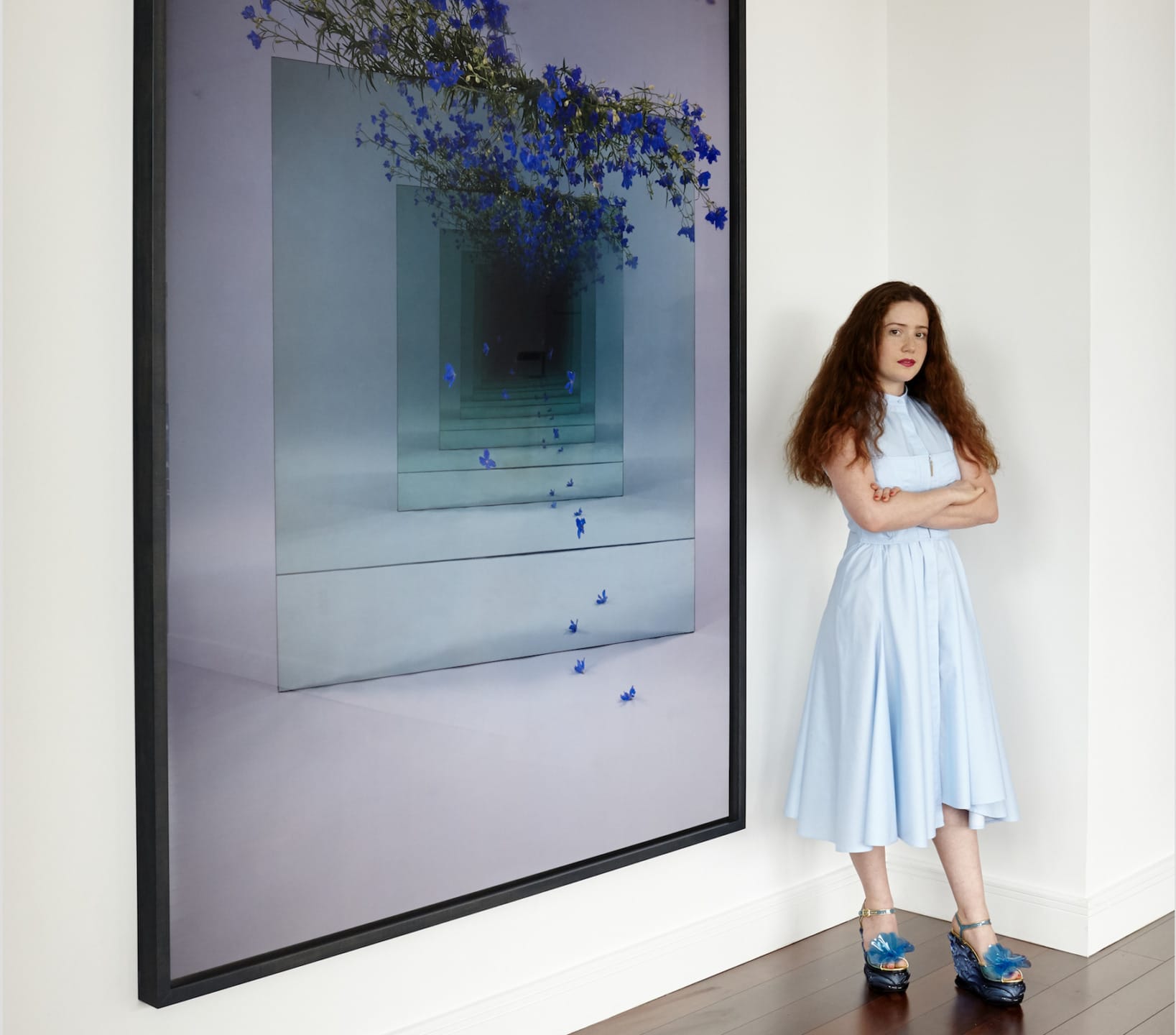 Person in a light blue dress standing beside a large artwork with blue flowers on a modern, abstract background.