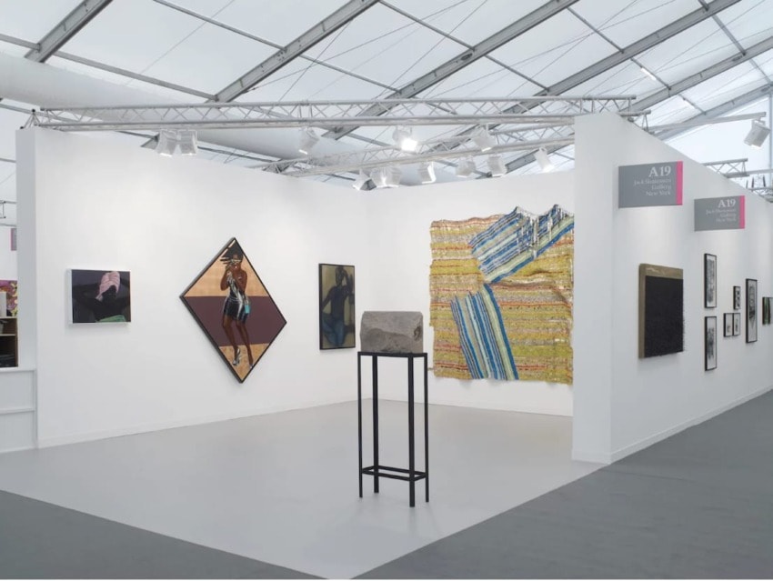 art exhibition booth showing various paintings and a sculpture on display against white walls in a gallery setting