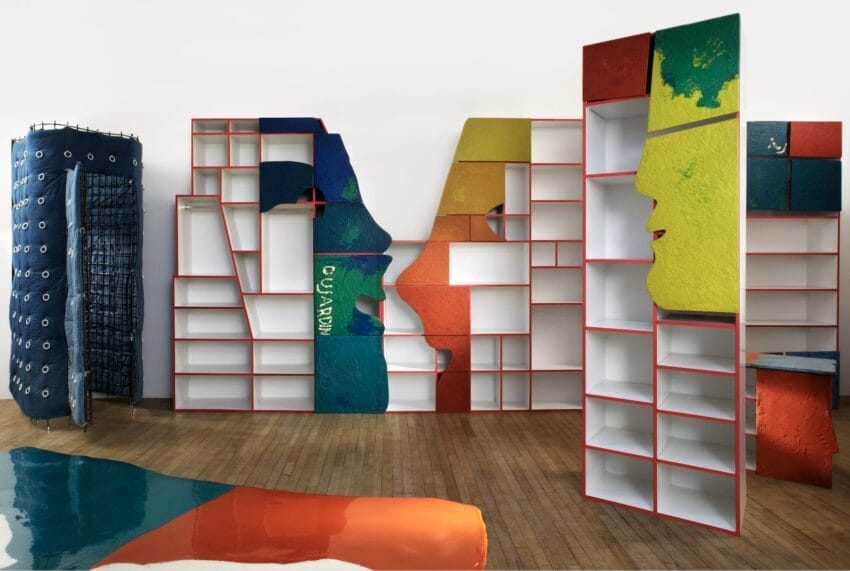 Colorful abstract art installation with face-shaped shelves and textured surfaces on wooden floor.