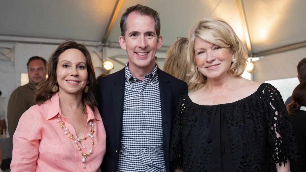 Three people smiling at an event under a tent with warm lighting.