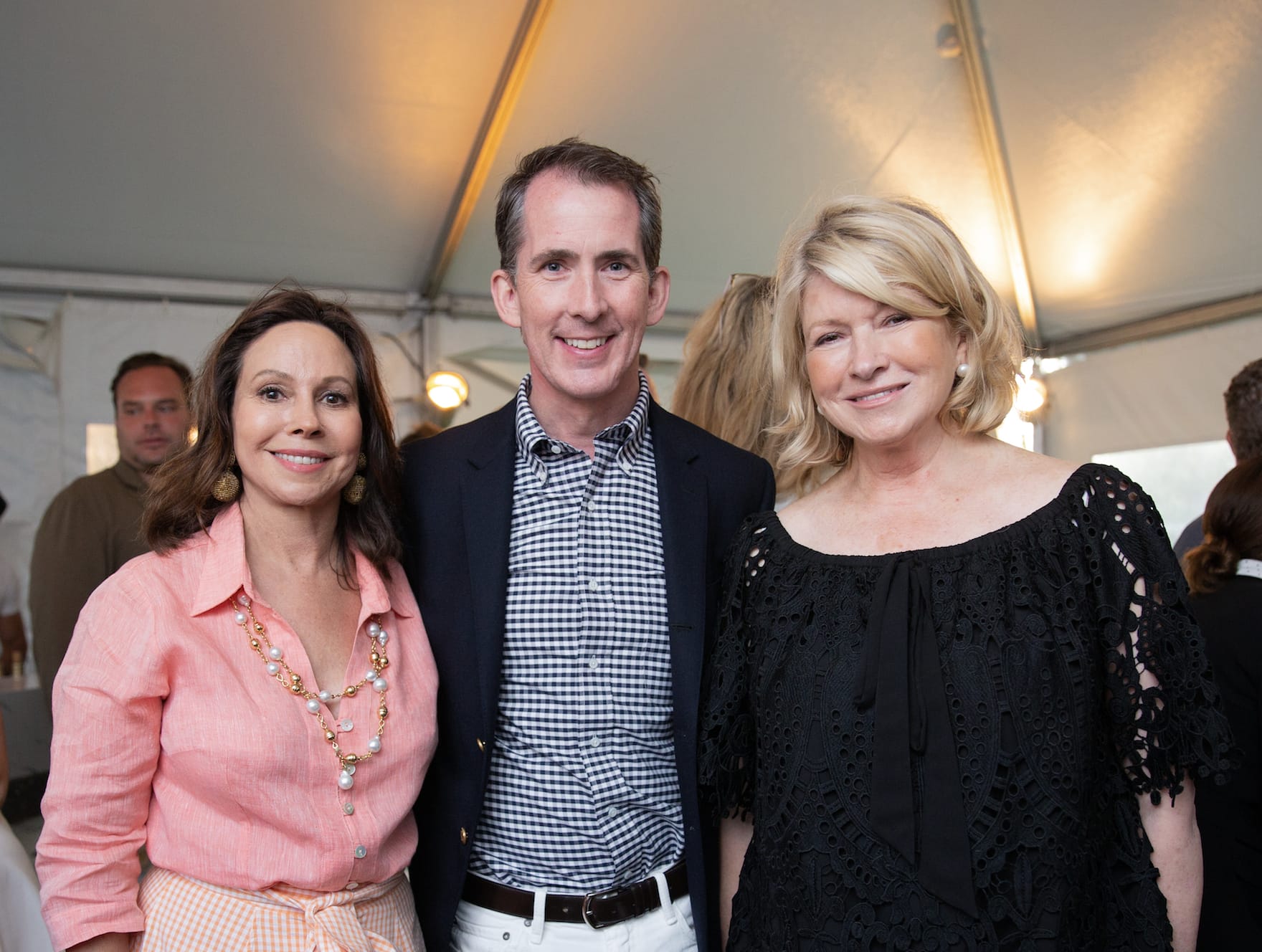 Three people smiling at an event under a tent with warm lighting.