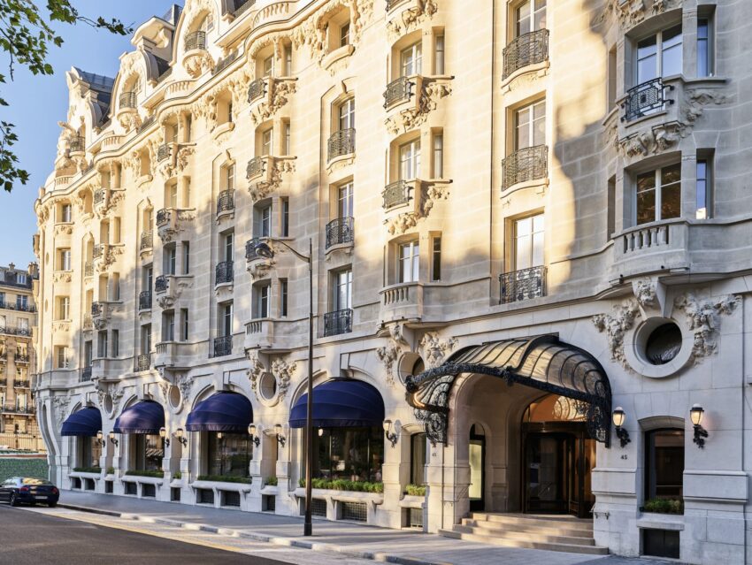 Elegant historic hotel facade with ornate architecture, blue awnings, and a grand entrance on a sunny day.