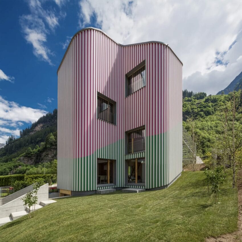 Colorful striped modern building with unique curved shape, set in a lush green landscape under a blue sky.