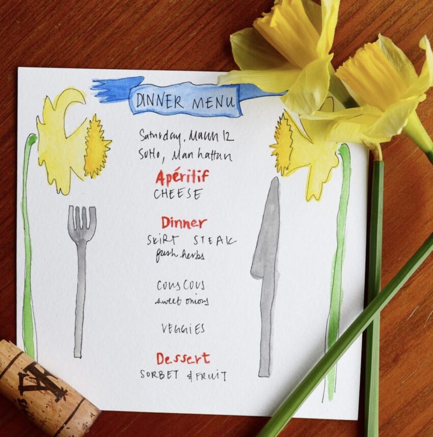 Handwritten dinner menu on a wooden table with daffodil flowers, wine cork, featuring cheese, steak, couscous, veggies, and dessert.