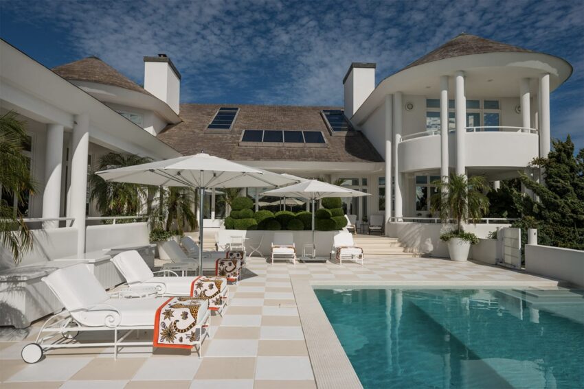 luxurious villa with pool, white lounge chairs, umbrellas, and tropical plants under a clear blue sky