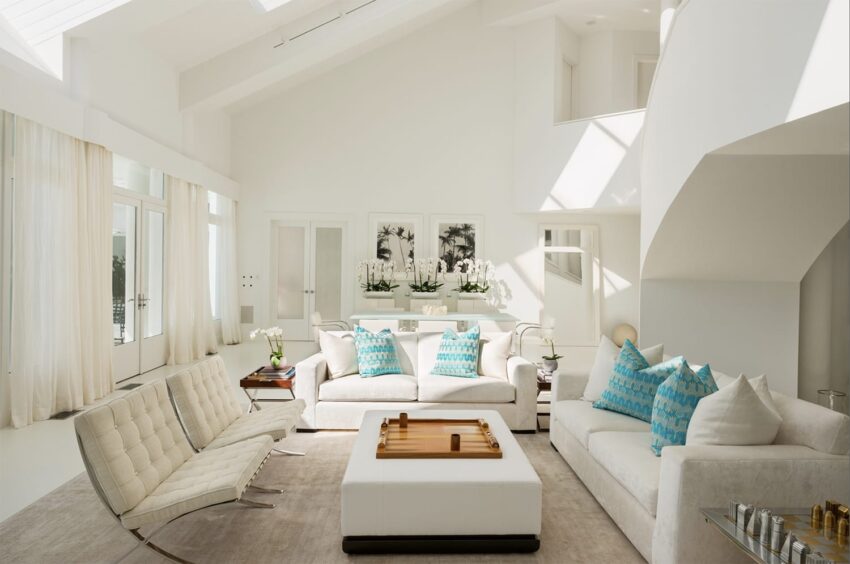 Spacious modern living room with white sofas, blue patterned pillows, and large windows letting in natural light.