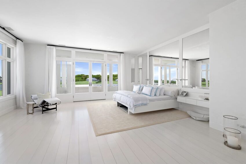 Bright, modern bedroom with white decor, large windows, and view of greenery.