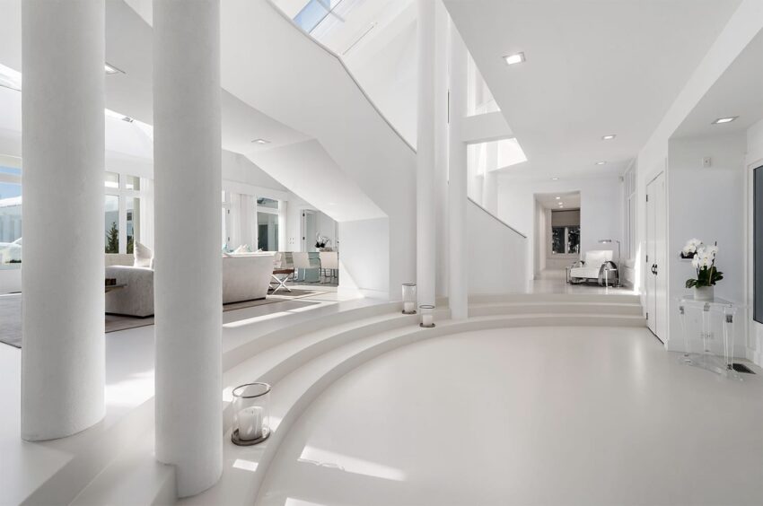 Spacious modern white interior with curved staircase, large windows, and minimalist furniture.