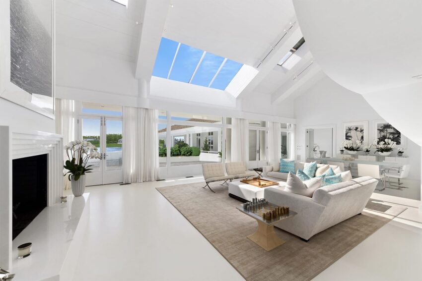 Spacious, white living room with large windows, modern furniture, and natural light streaming in from skylights.