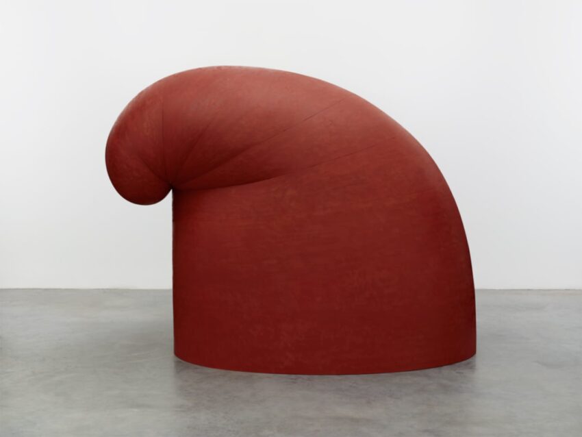 Large red abstract sculpture in a gallery with smooth curves and a rounded form against a neutral background.