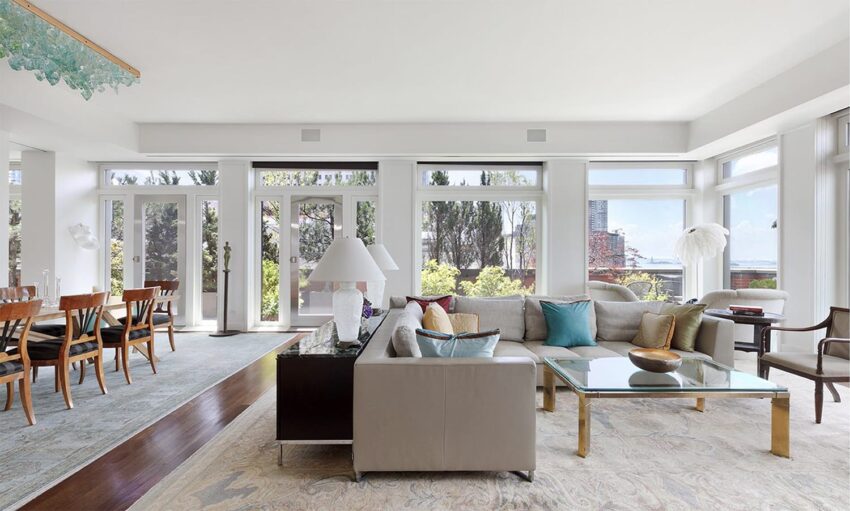 Spacious modern living room with large windows, neutral decor, and a dining area in the background.