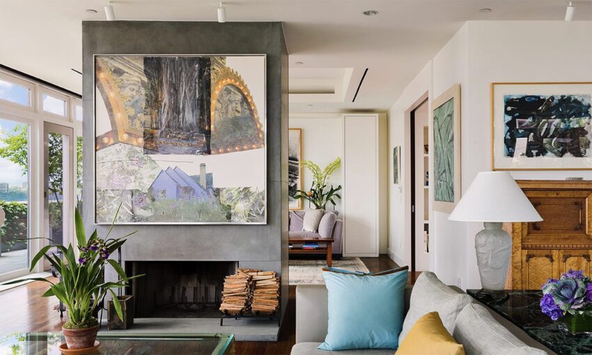 Modern living room with large abstract art above a fireplace, a gray sofa, and indoor plants near the window.