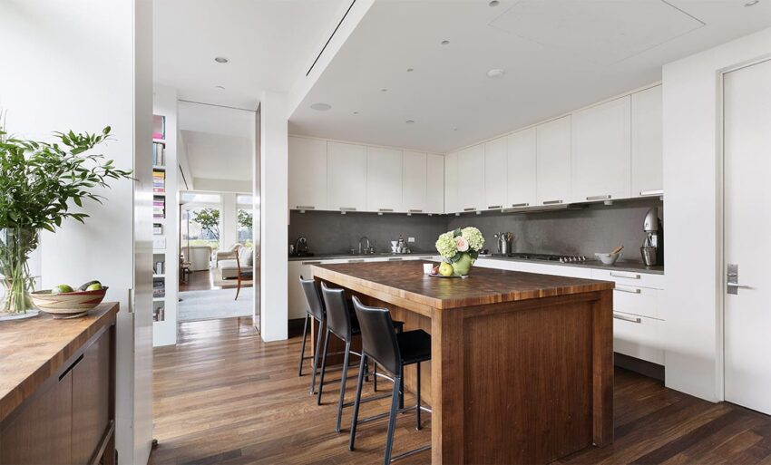 Modern kitchen with wooden island, bar stools, white cabinets, and a vase on the countertop.