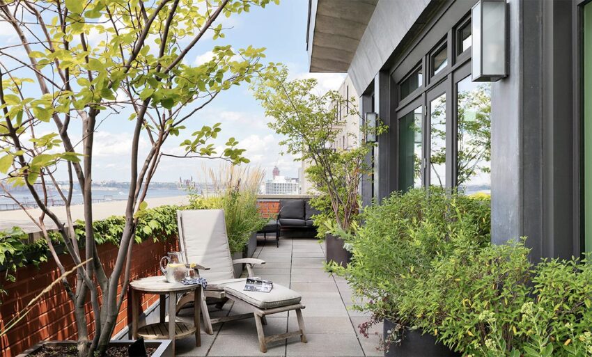 Rooftop terrace with plants and a seating area overlooking a cityscape under a blue sky.