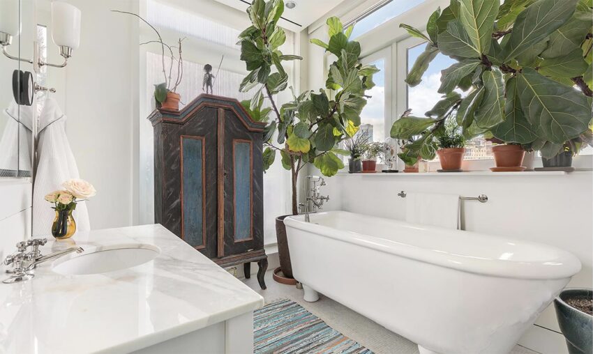 Bright bathroom with a vintage bathtub, wooden cabinet, large windows, and lush green plants.