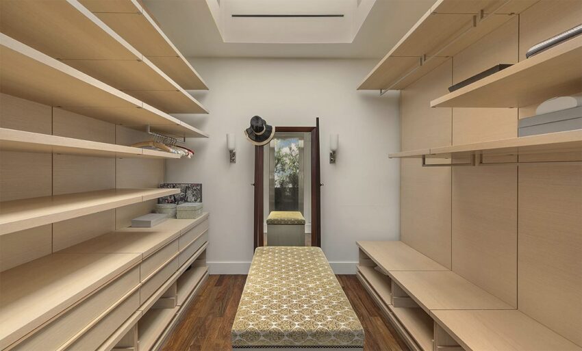 empty walk-in closet with wooden shelves and a bench in the center, mirror on the far wall, hardwood floor