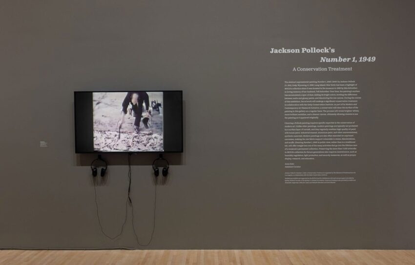 Exhibit display of Jackson Pollock's art conservation process with a screen showing video and headphones on a gallery wall.