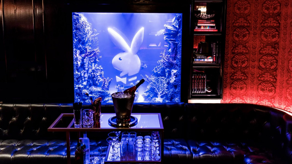 Elegant lounge with a blue-lit aquarium, featuring a rabbit figure, plush seating, and a table set with drinks.