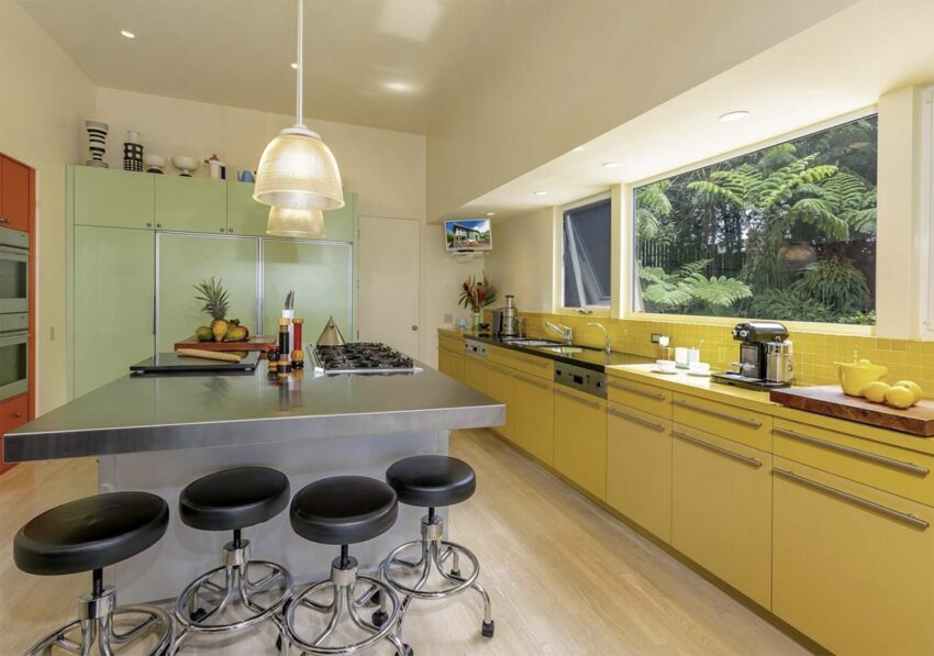 Modern kitchen with yellow cabinets, large window view, and stainless steel island with barstools.