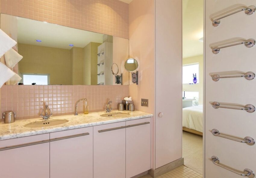 Modern bathroom with two sinks, large mirror, and pink tiles, adjacent to a bedroom with natural light streaming in.