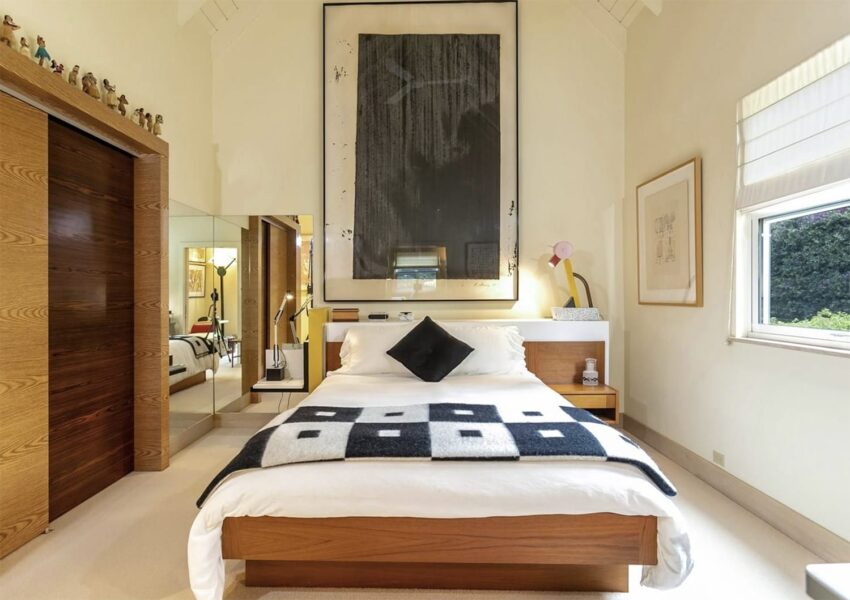 Modern bedroom with wooden furniture, large abstract painting above bed, and geometric-patterned blanket on bed.