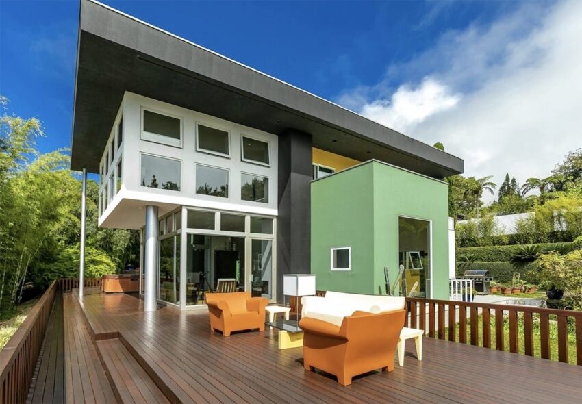 Modern house with large windows, green accent wall, and wooden patio deck featuring orange and white outdoor furniture.