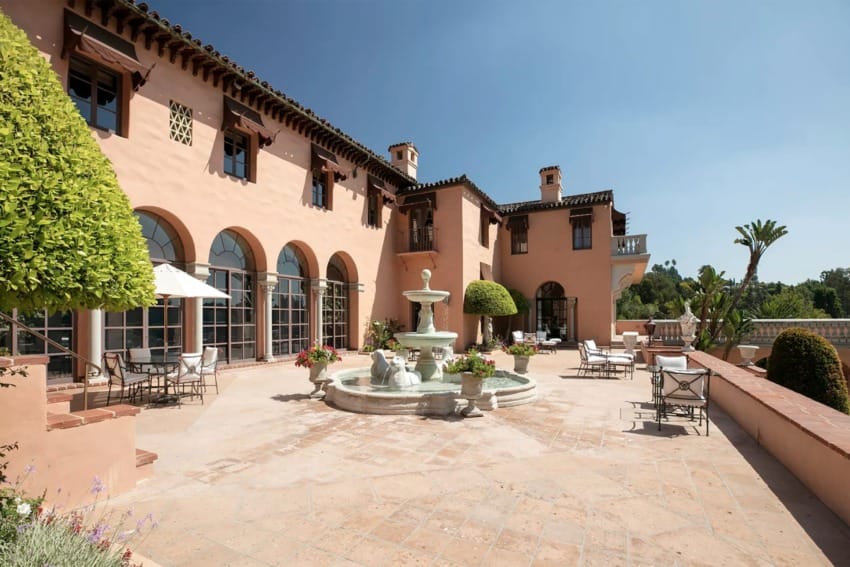 Spanish-style villa with terracotta walls, arched windows, and a central fountain on a spacious outdoor patio.