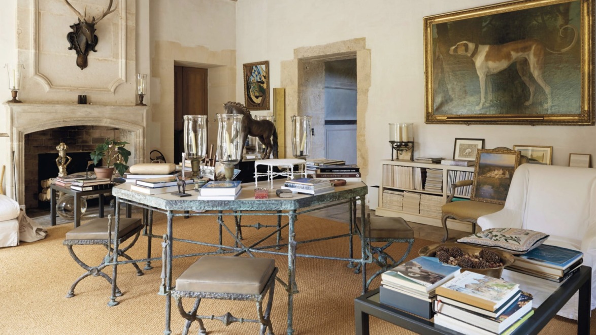 Elegant study room with a round metal desk, upholstered chairs, fireplace, books, and decorative artwork on the walls.