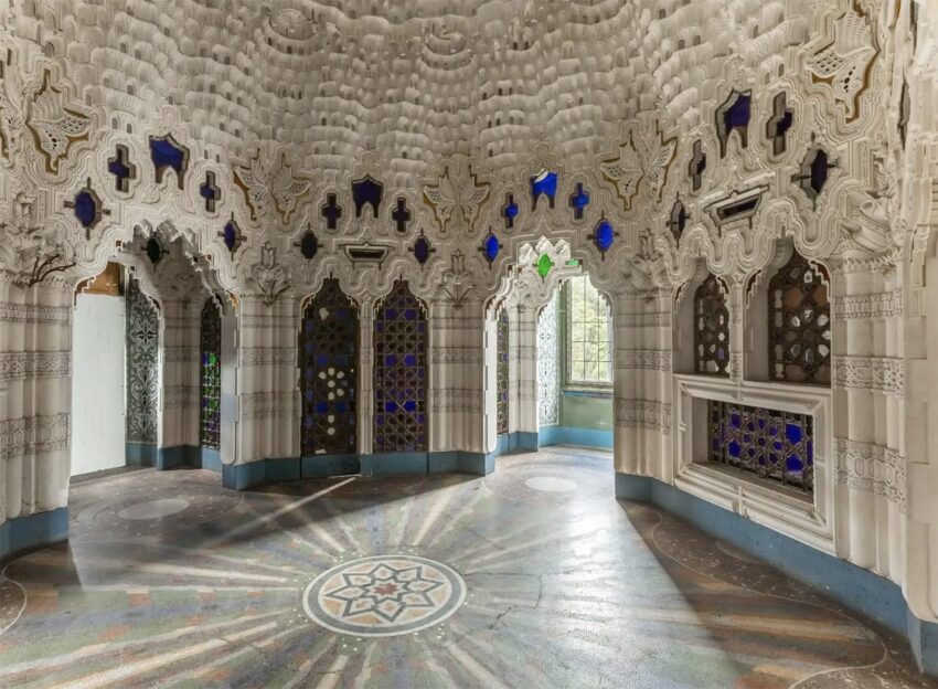 Ornate room with intricate white stucco walls, colorful stained glass windows, and a decorative star pattern on the floor.