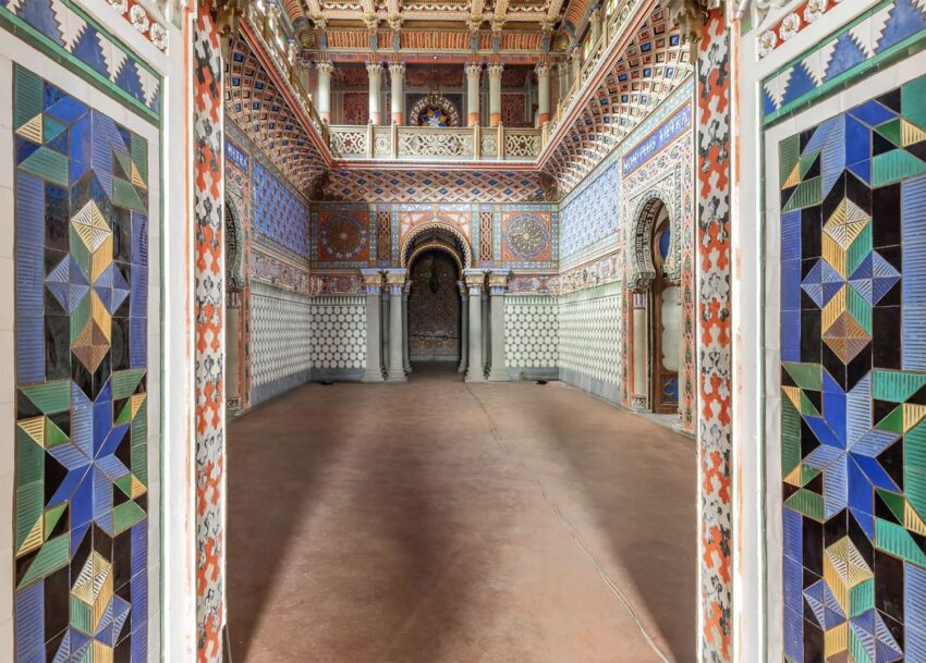 Intricately decorated interior with colorful geometric patterns on walls and ceiling, featuring arches and columns.