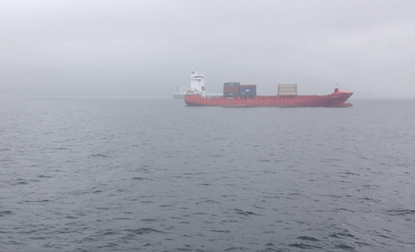 Large red cargo ship carrying containers on a foggy ocean.