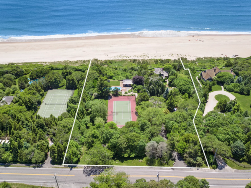 Aerial view of a beachfront property with tennis courts, green trees, and houses along a sandy beach.
