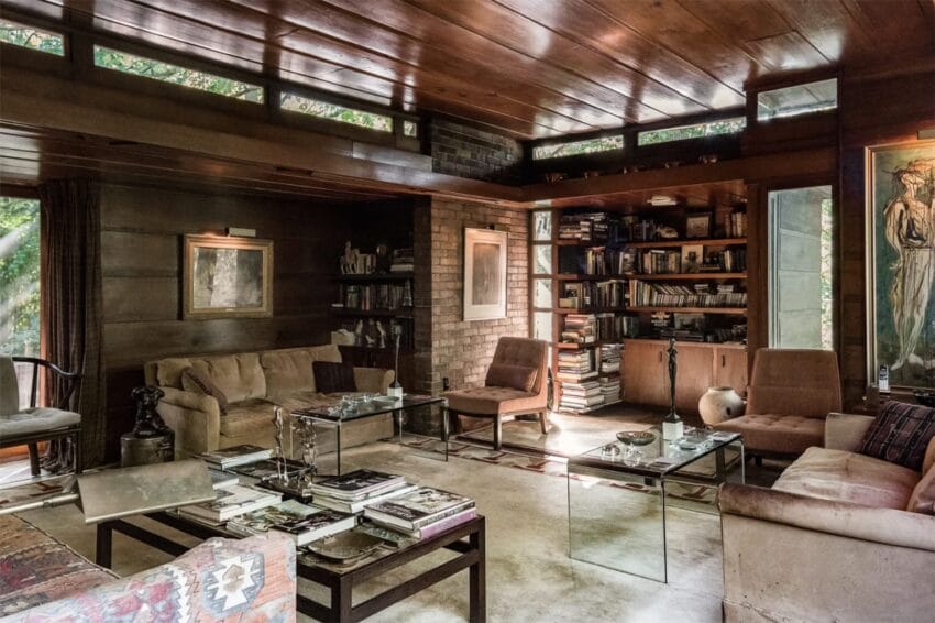 Cozy living room with wooden paneling, bookshelves, and glass coffee tables surrounded by sofas and chairs.