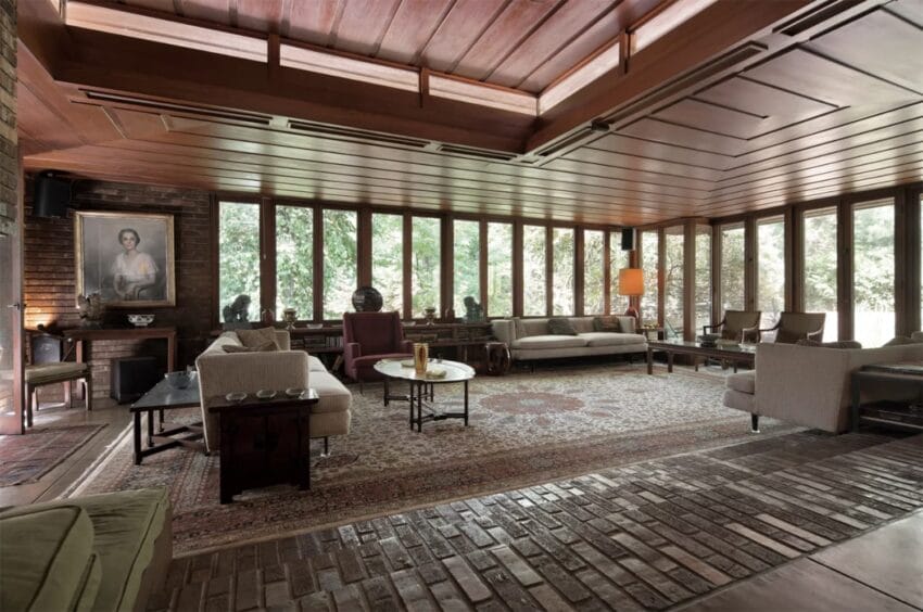 Spacious living room with wooden ceiling, large windows, and elegant furniture, featuring a painting and lush garden view.