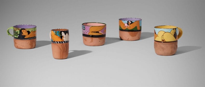 Colorful ceramic mugs and cups with artistic painted figures on neutral background.