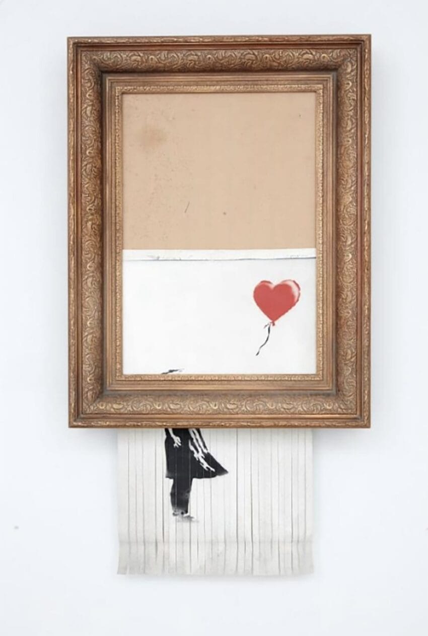 Artwork in ornate frame with partially shredded paper showing figure holding a red heart-shaped balloon.