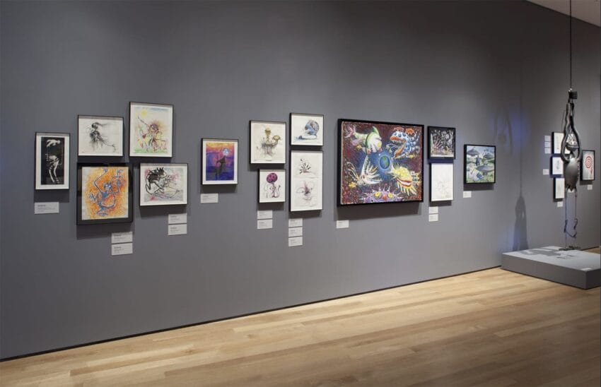 Art gallery wall displaying various framed artworks and paintings with a spotlight illuminating one exhibit in a modern setting.