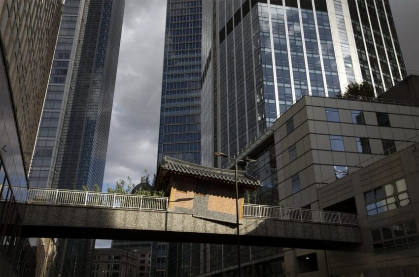 Traditional Korean structure on a bridge surrounded by modern skyscrapers under a cloudy sky.