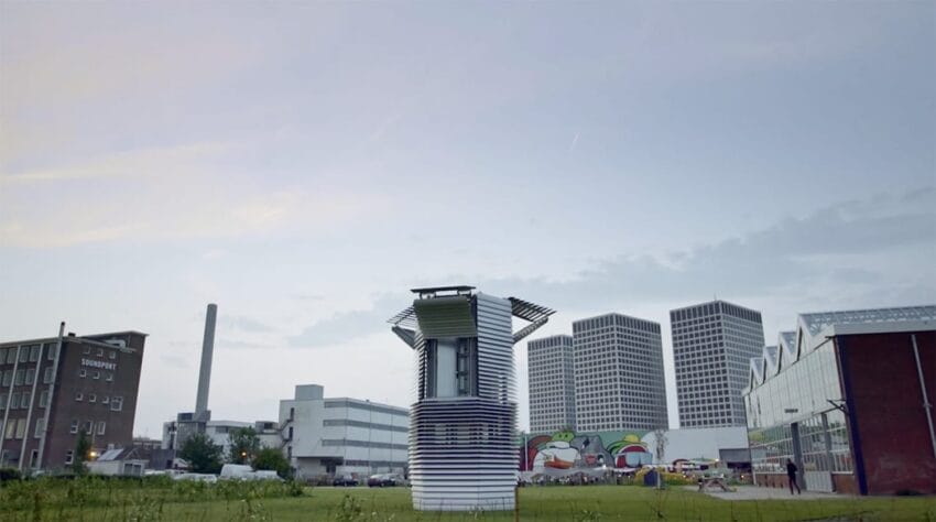 Large outdoor air purifier tower in a city landscape with several modern buildings and a colorful mural in the background