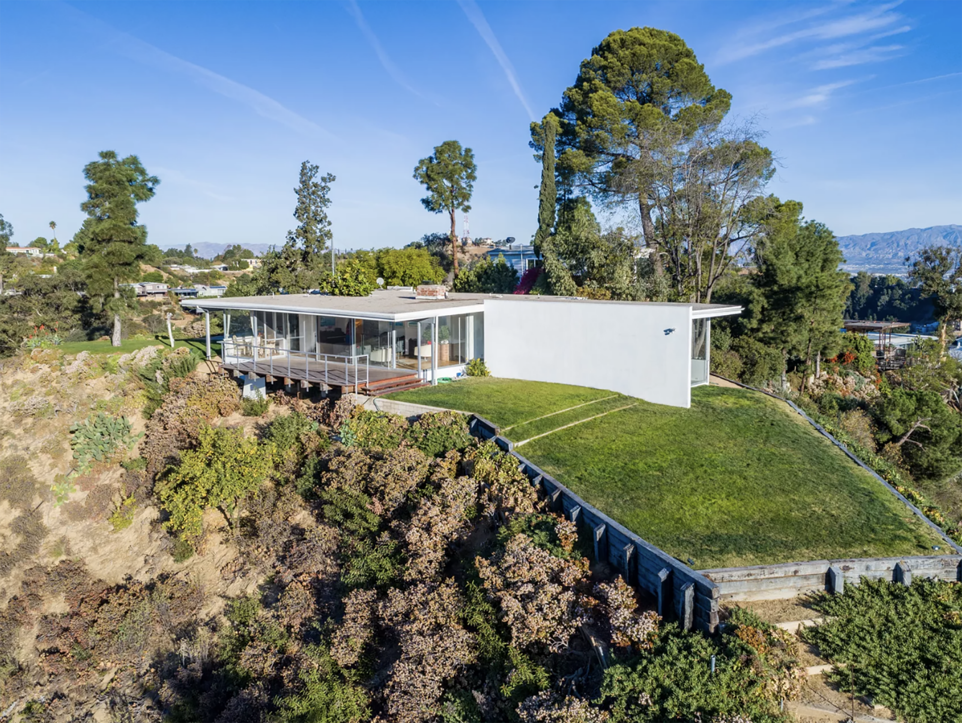 Mid-century modern house on hillside with large windows, surrounded by trees and overlooking a scenic view