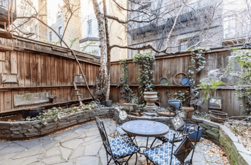 Cozy backyard patio with a stone floor, wooden fencing, and outdoor furniture surrounded by trees and plants.