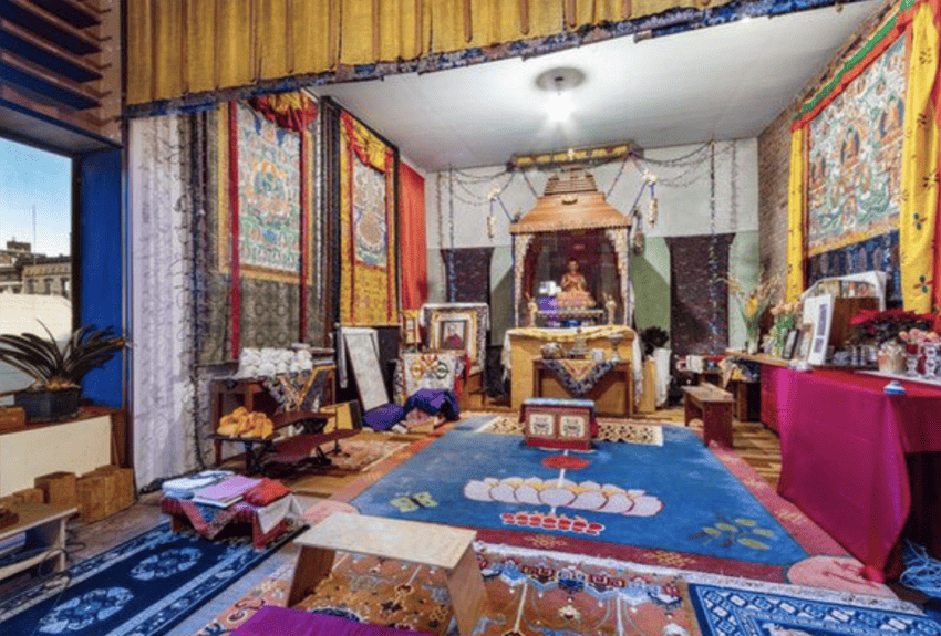 Colorful Tibetan altar room with vibrant tapestries, sacred objects, and meditation cushions on patterned carpets.