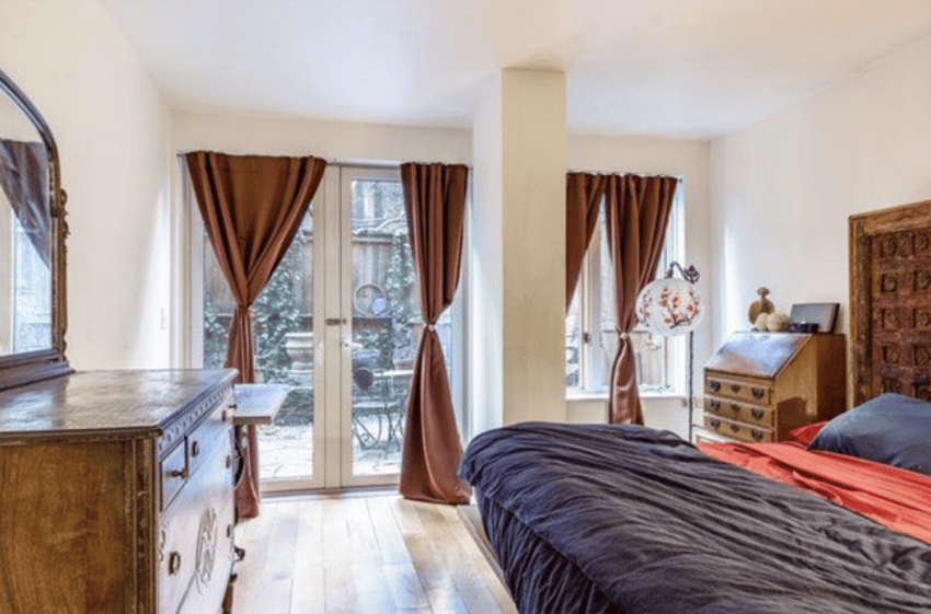 Cozy bedroom with wooden furniture, dark curtains, and natural light from large windows overlooking a patio.